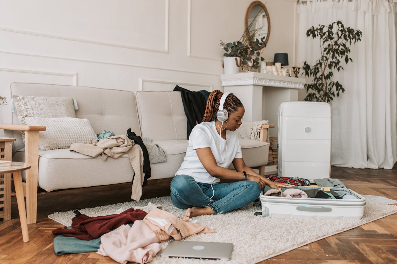 A woman with headphones packing a suitcase in her stylish living room, preparing for travel.